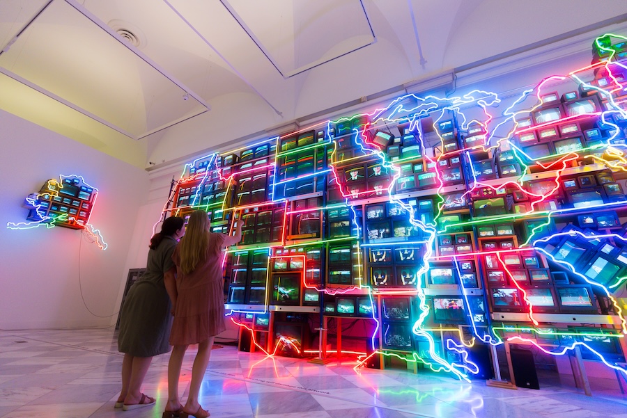 Two people look at a large, neon art installation that replicates the U.S.