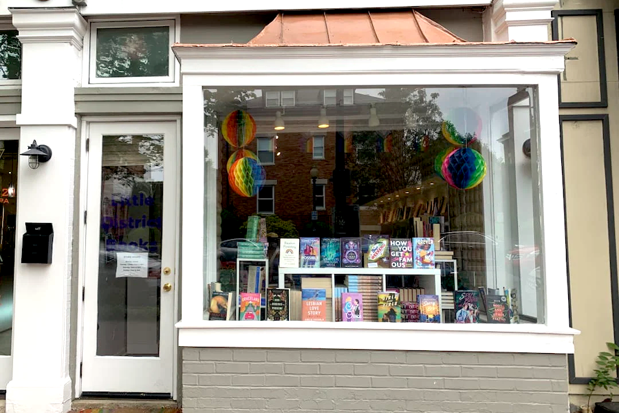 An exterior window of a small bookstore with rainbow pride decorations and books displayed inside. 