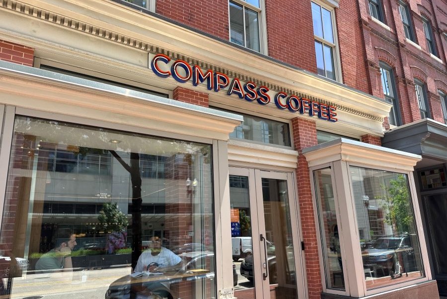 Exterior view of Compass Coffee with glass windows, people inside, and the storefront sign visible on a sunny day