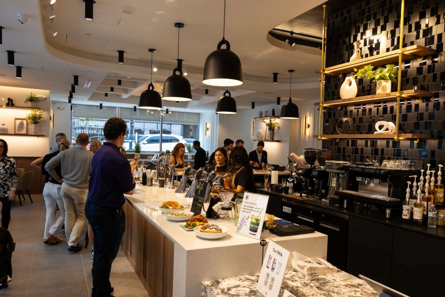 Interior of For Five Coffee shop with customers ordering at the counter, baristas preparing drinks, and modern decor with hanging lights and shelves.