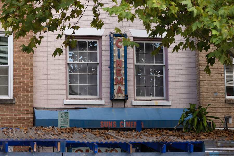 The retro Suns Cinema sign hangs between two windows on a light pink brick building.