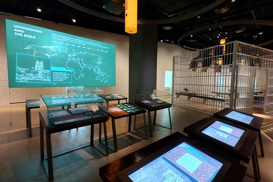 Exhibit at the Museum of the Bible featuring interactive displays on the history of the Bible in universities and a reconstructed prison cell.