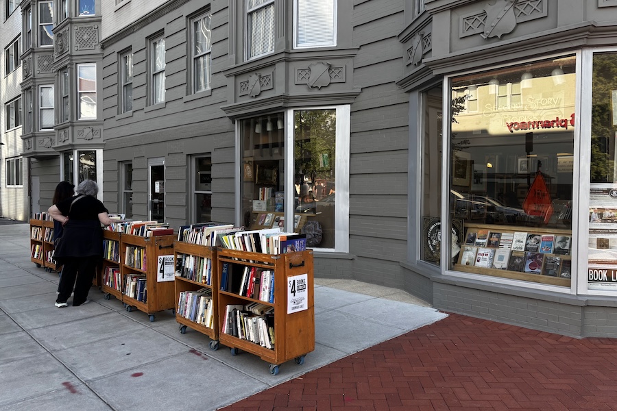 Two people browse rolling carts of discounted books outside Second Story Books.
