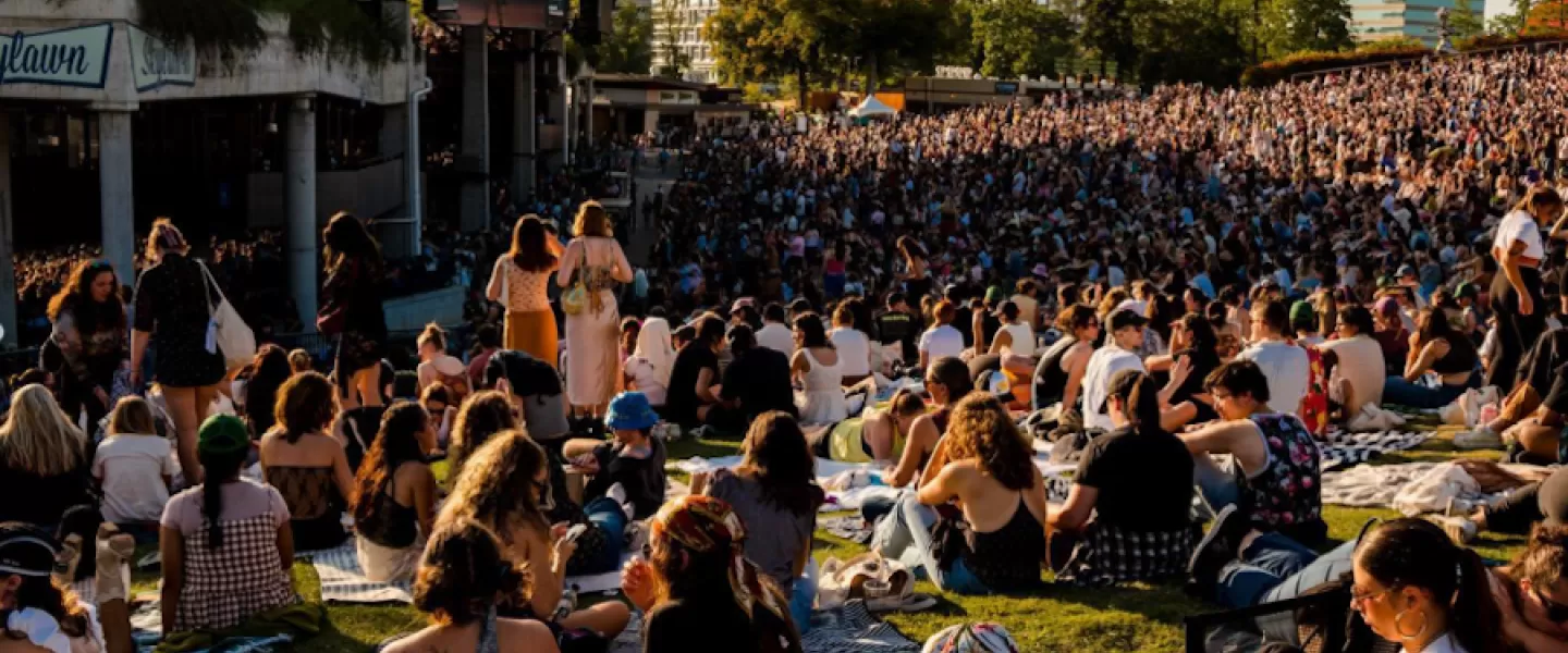 concertgoers seated on the lawn in front of a pavilion