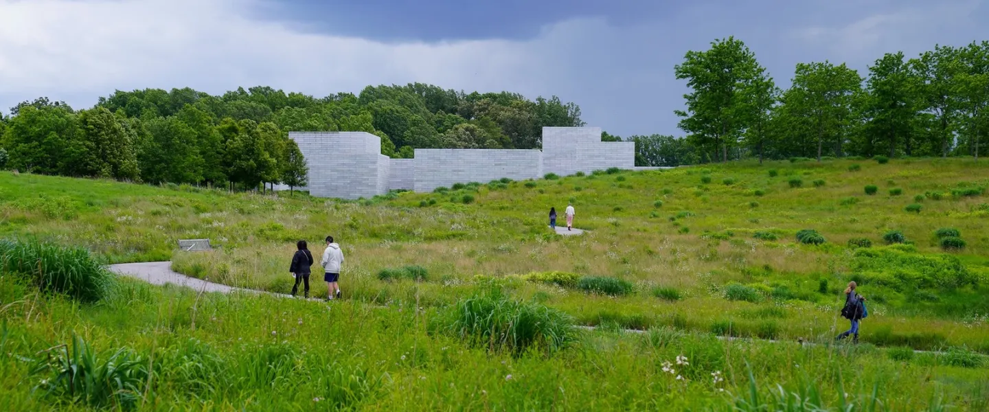 Visitors walk along a winding path through green meadows toward the Pavilions at Glenstone Museum.