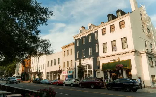A picturesque Georgetown streetscape featuring charming historic buildings with boutique shops and parked cars, bathed in late afternoon sunlight under a clear sky.

