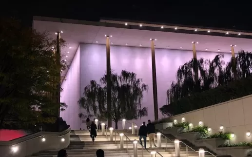 Nighttime view of the Kennedy Center's outdoor stairs, with people walking up and the building illuminated in soft purple lights.