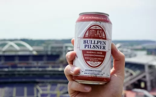 A hand holds a beer can with a view of Nationals Park in the background. 
