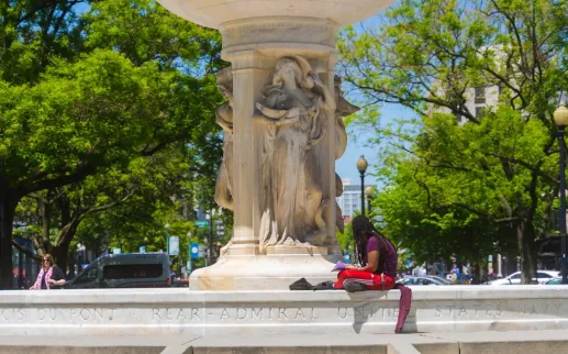 A man sits on the edge of the Dupont Circle fountain with a book on a sunny afternoon.