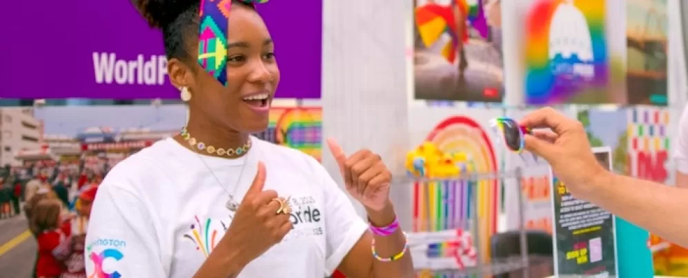 A young woman with a rainbow bow in her hair plays a game with an attendee at an event booth.