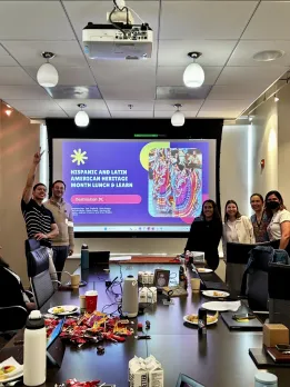 A group of coworkers smiles in front of a presentation screen during a Hispanic and Latin American Heritage Month lunch and learn at Destination DC.
